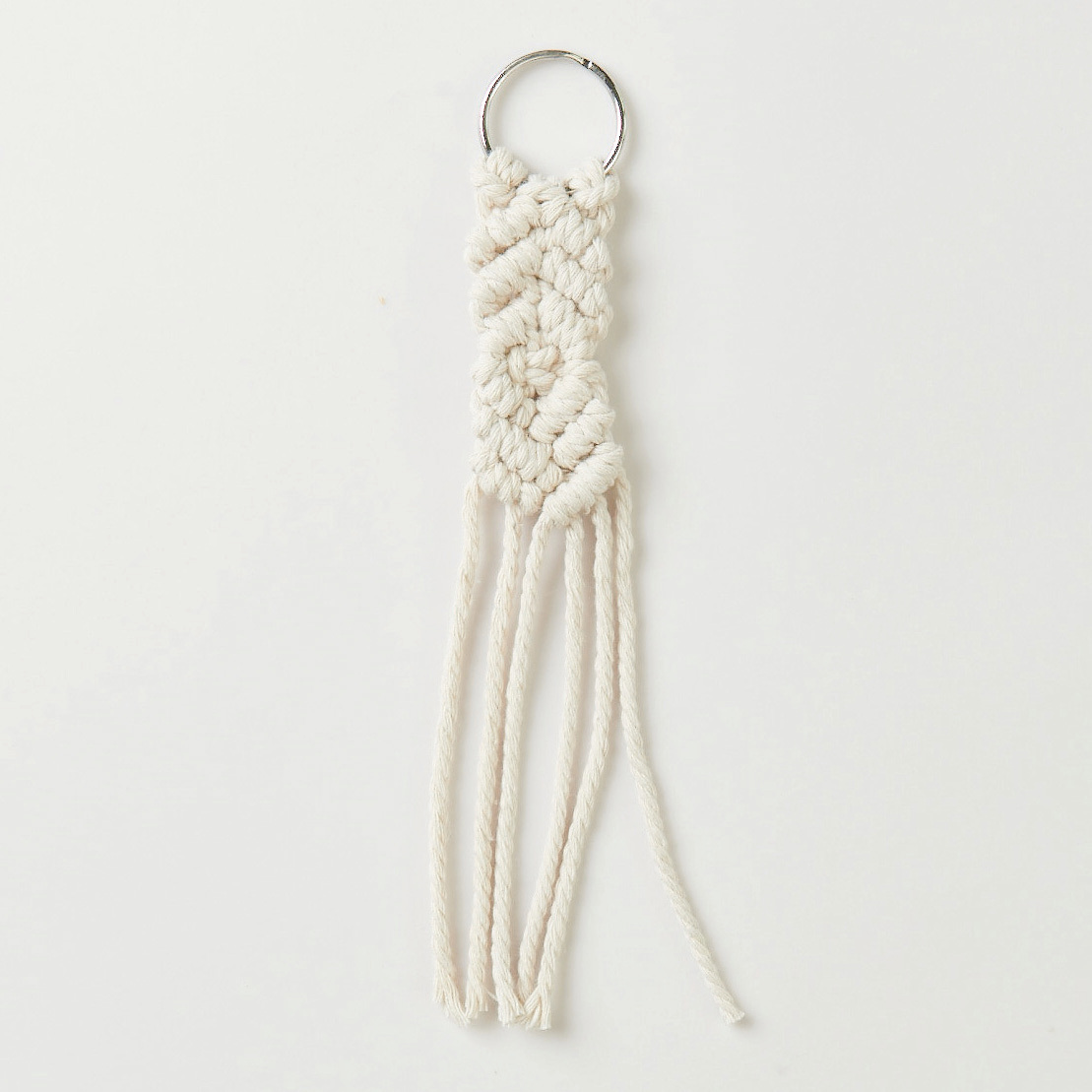 Set de macramé porte-clés 3 pièces from Rico Design Makramee Set Schlüsselanhänger von Rico Design, zeigt einen cremefarbenen Anhänger mit geflochtenem Muster und Fransen.