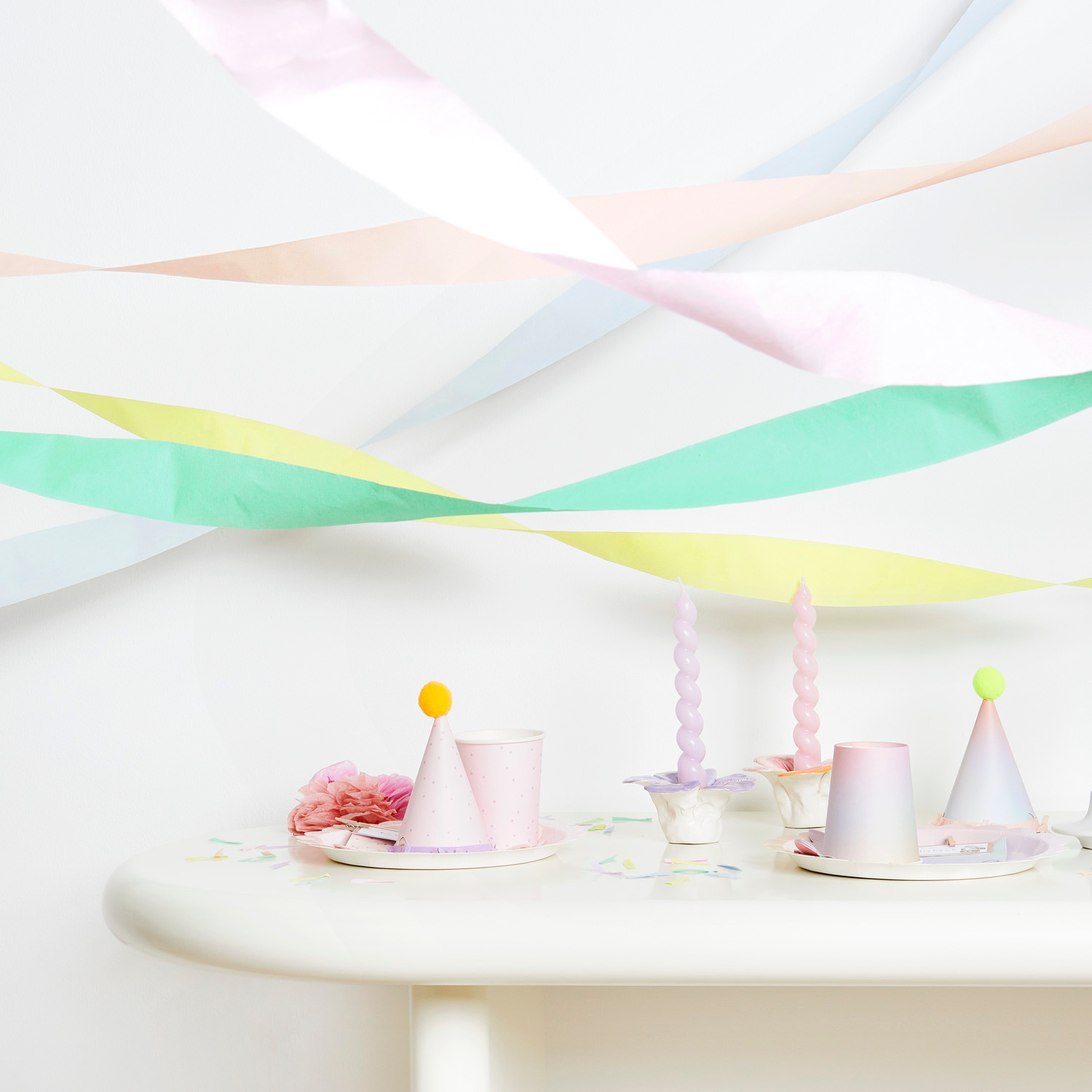 Kreppbänder extra breit Regenbogen Pastell Mix 5,5cmx10m 9 Stück von Rico Design Kreppbänder extra breit Regenbogen Pastell Mix dekorieren einen Tisch mit Partyhüten und Kerzen.