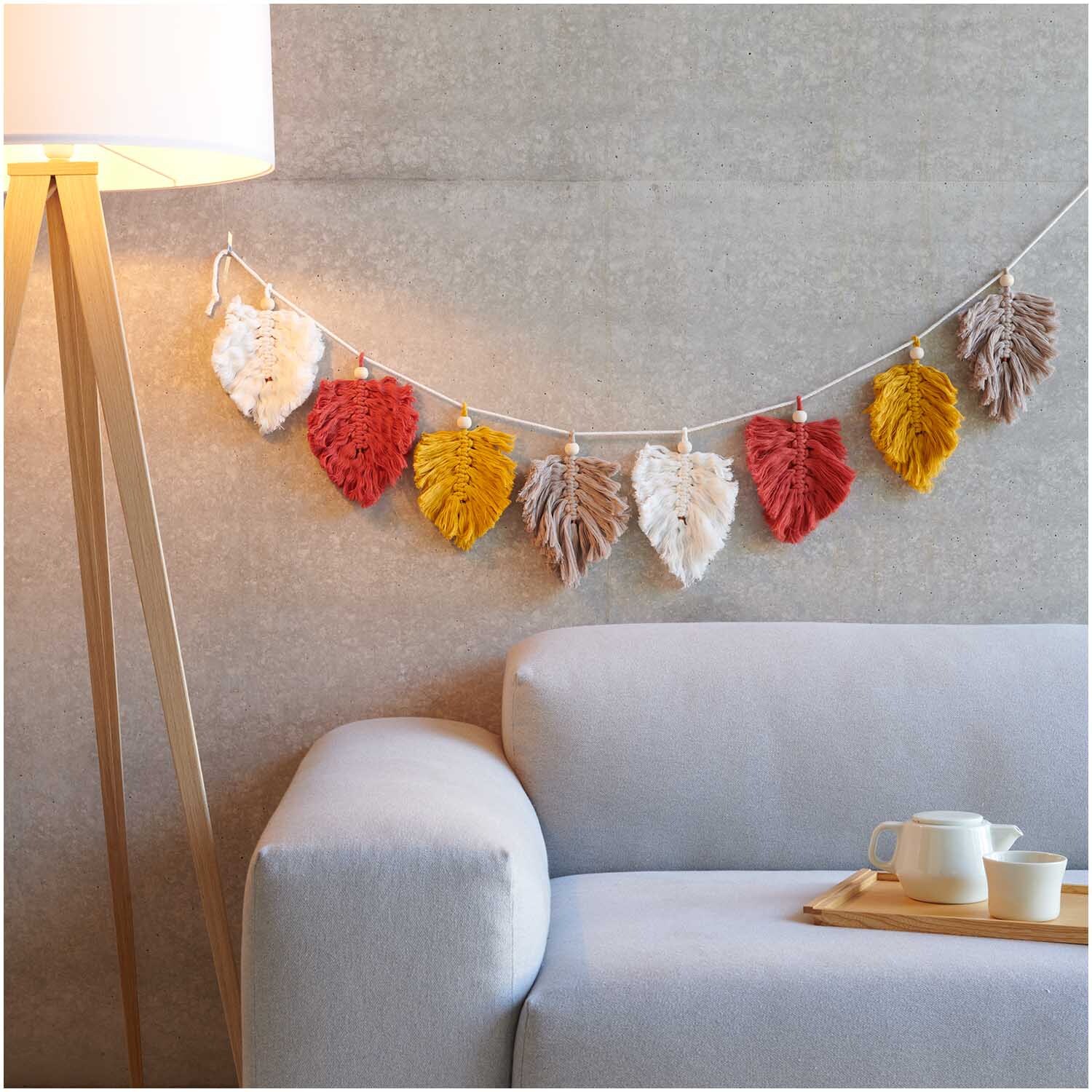Creative Cotton Cord Makramee-Garn von Rico Design in verschiedenen Farben, dekorativ als Blättergirlande über einem Sofa aufgehängt.