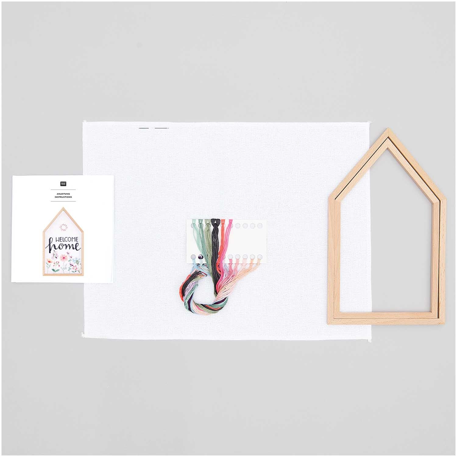 Stickpackung Welcome Home groß: Komplettset mit Garn, Anleitung und Holzrahmen von Rico Design auf grauem Hintergrund.